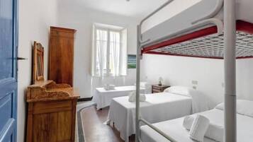 A hotel room with bunk beds, a wooden dresser, a small table, and a window with curtains.