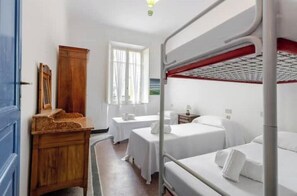 A hotel room with bunk beds, a wooden dresser, a small table, and a window with curtains. - Hostdomus - Cherry Home (Alassio)