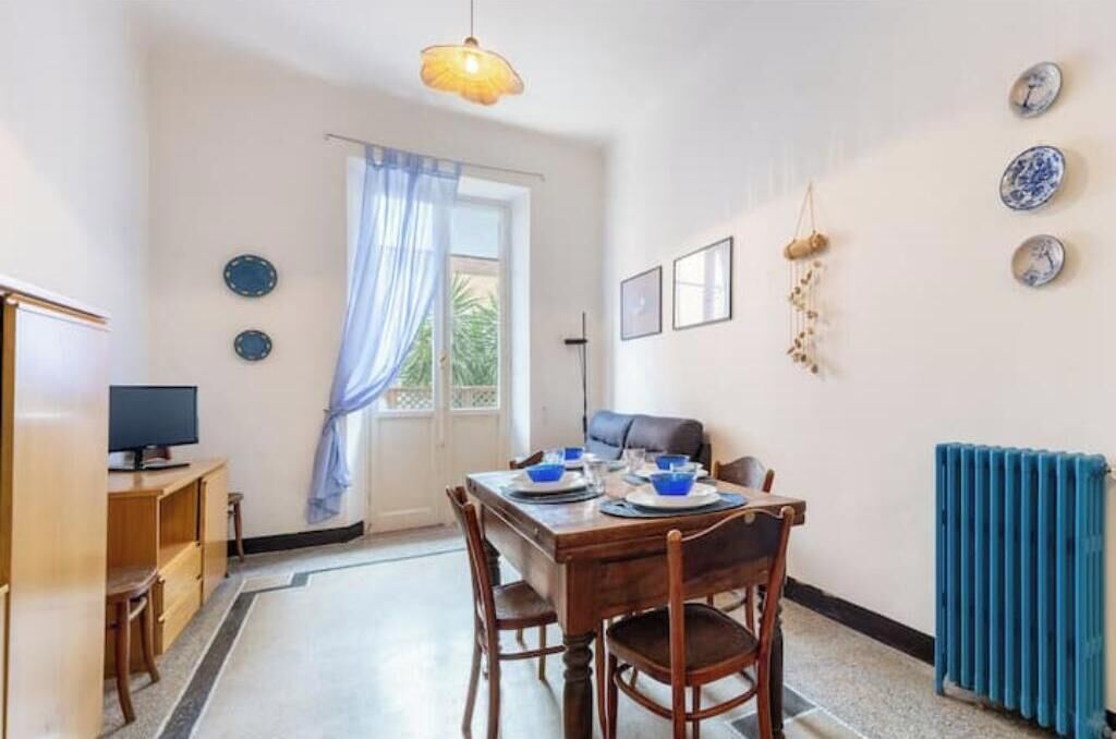 A dining area with a table set for two, a television on a stand, and a window with curtains.