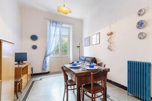 A dining area with a table set for two, a television on a stand, and a window with curtains. - Hostdomus - Cherry Home (Alassio)