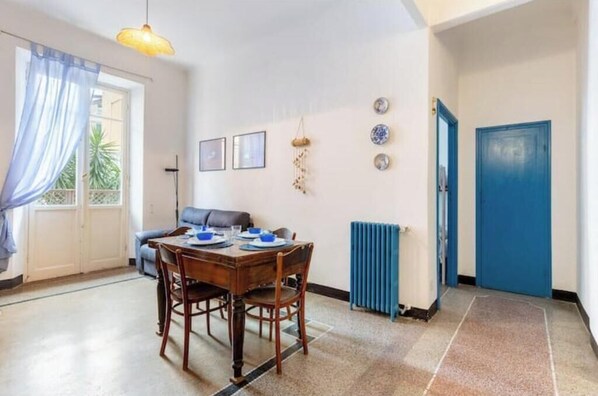 A dining area with a table set for two, a blue door, and a radiator. - Hostdomus - Cherry Home (Alassio)