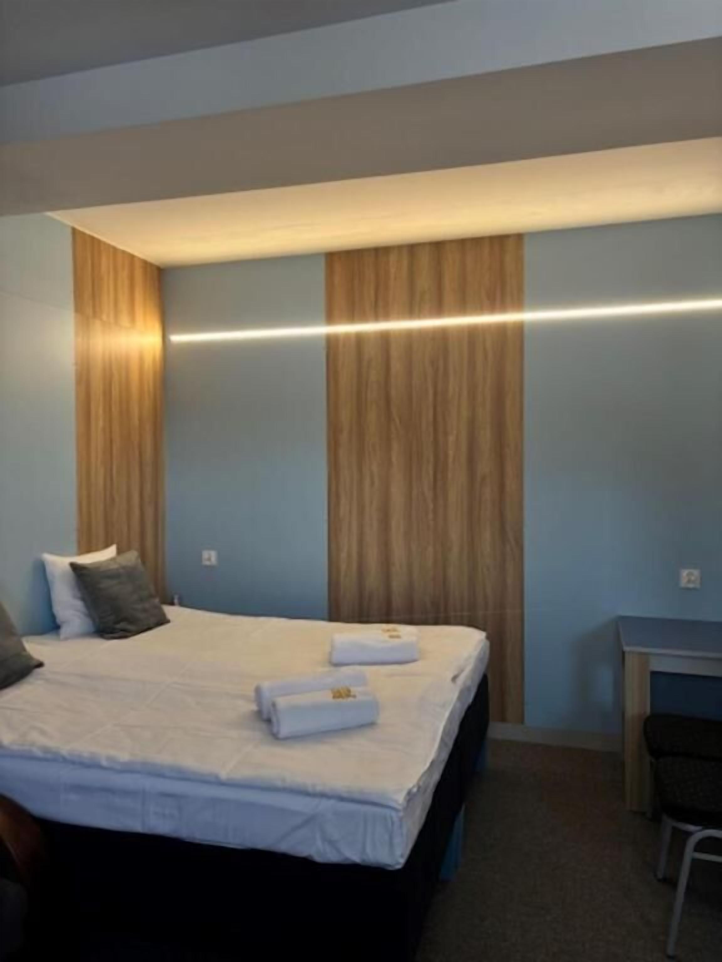 Hotellihuone, jossa on sänky, tyynyjä, työpöytä ja tuoli.