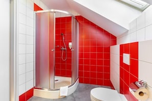 Ein modernes Badezimmer mit einer Duschkabine aus Glas, einer Toilette und roten Fliesen.
