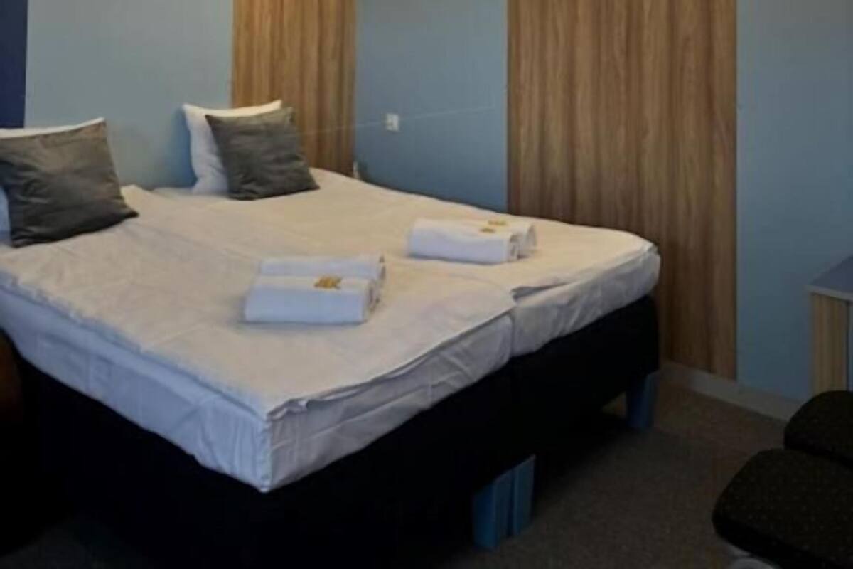 A modern hotel room with a large bed, wooden paneling on the walls, and a bedside table.