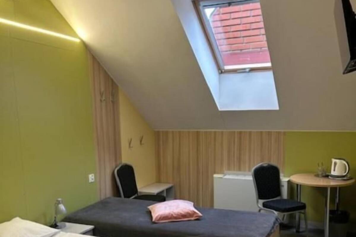A room with two beds, a desk, a chair, a small table with a kettle, and a skylight.