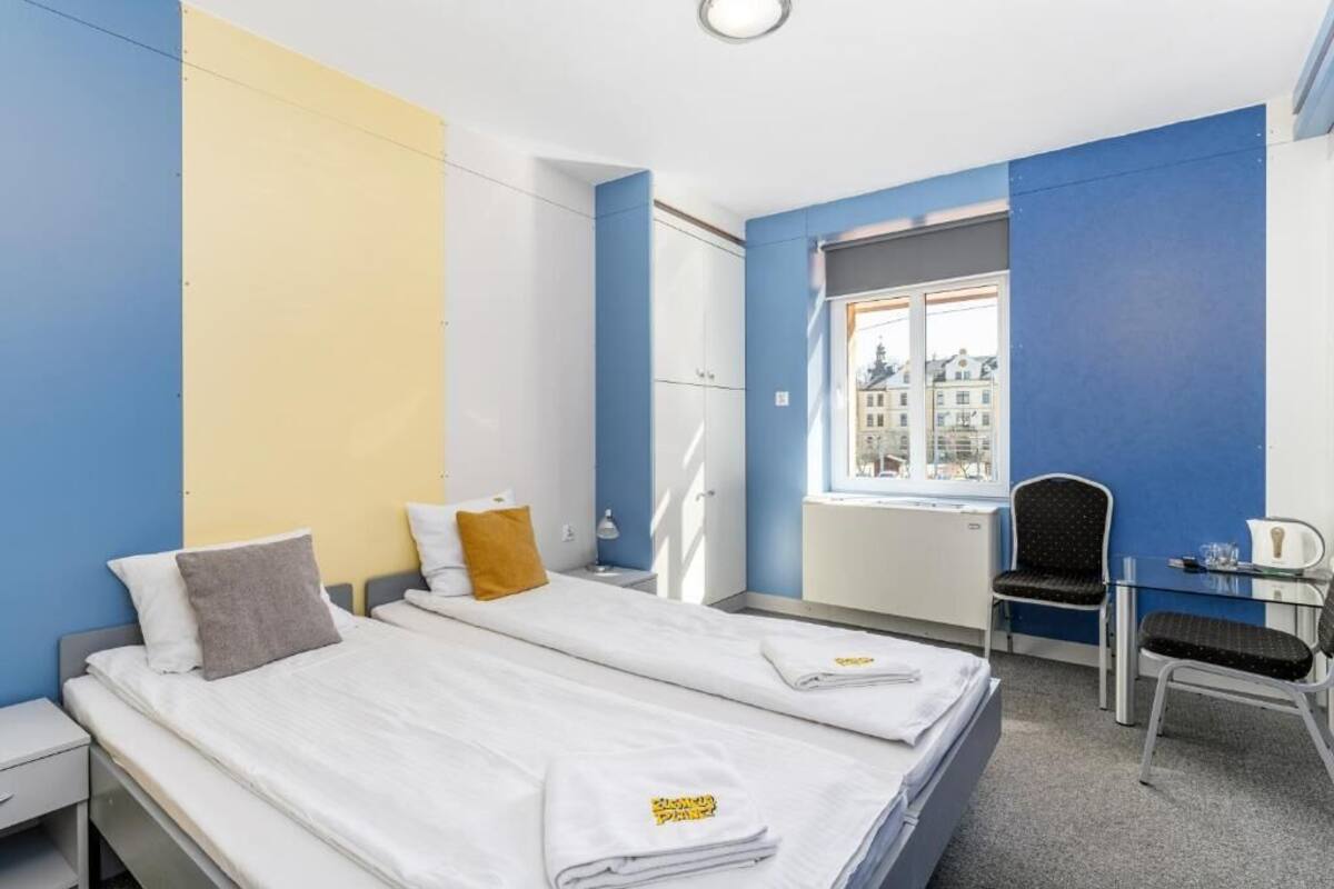 A hotel room with two beds, a desk, a chair, and a window with a city view.
