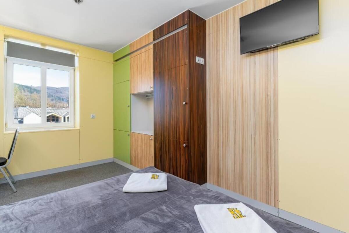 A room with a bed, a chair, a window with a view, a wardrobe, and a TV mounted on the wall.