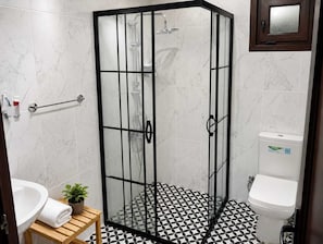 A bathroom with a glass-enclosed shower, a white toilet, a sink with a marble countertop, and a patterned floor. - Agva Tartaruga Motel (Sile)