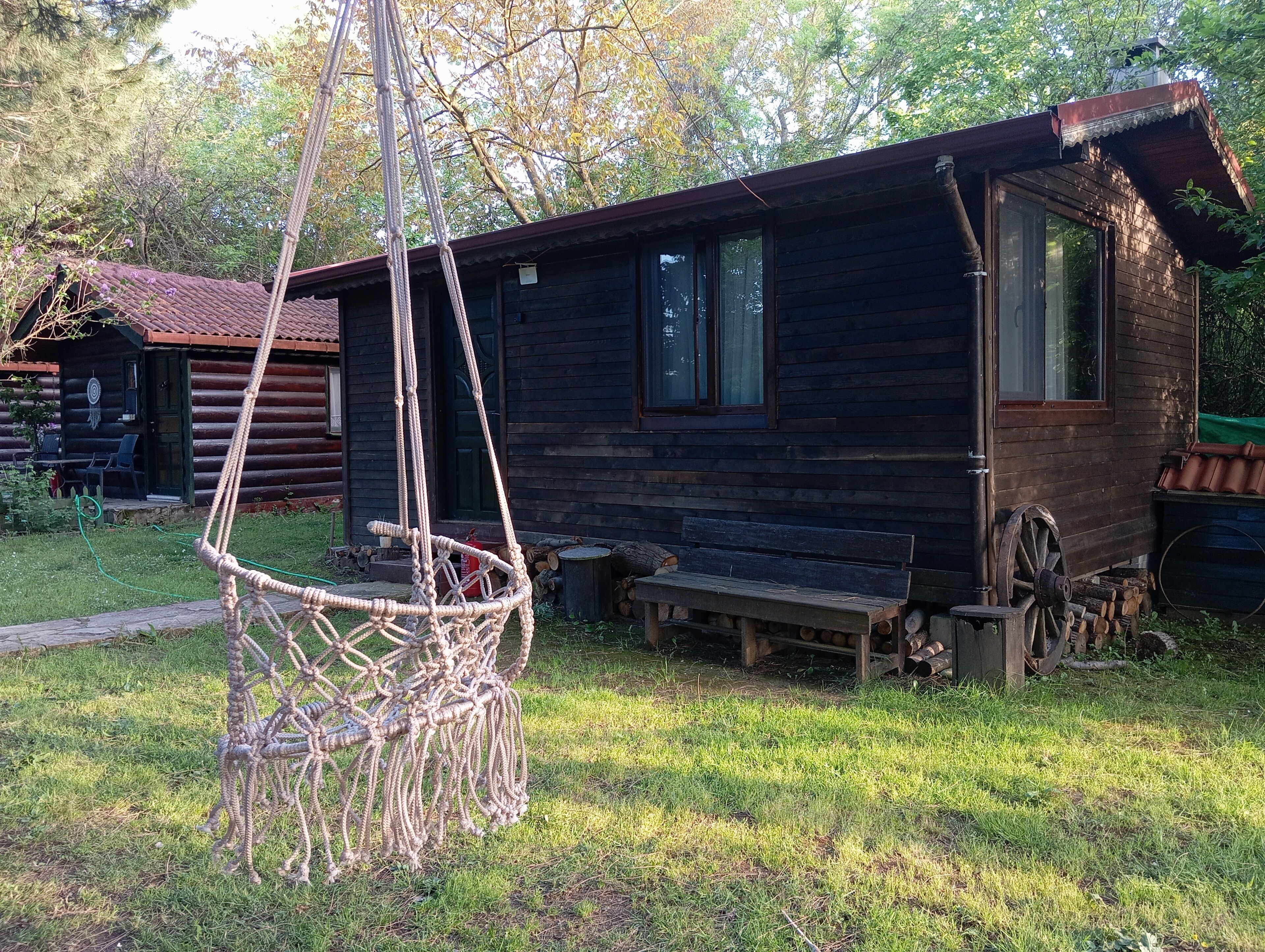 A rustic wooden cabin with a rope swing, a bench, and a wheelbarrow.