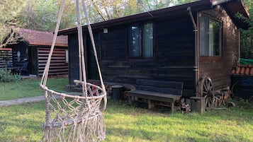 A rustic wooden cabin with a rope swing, a bench, and a wheelbarrow.