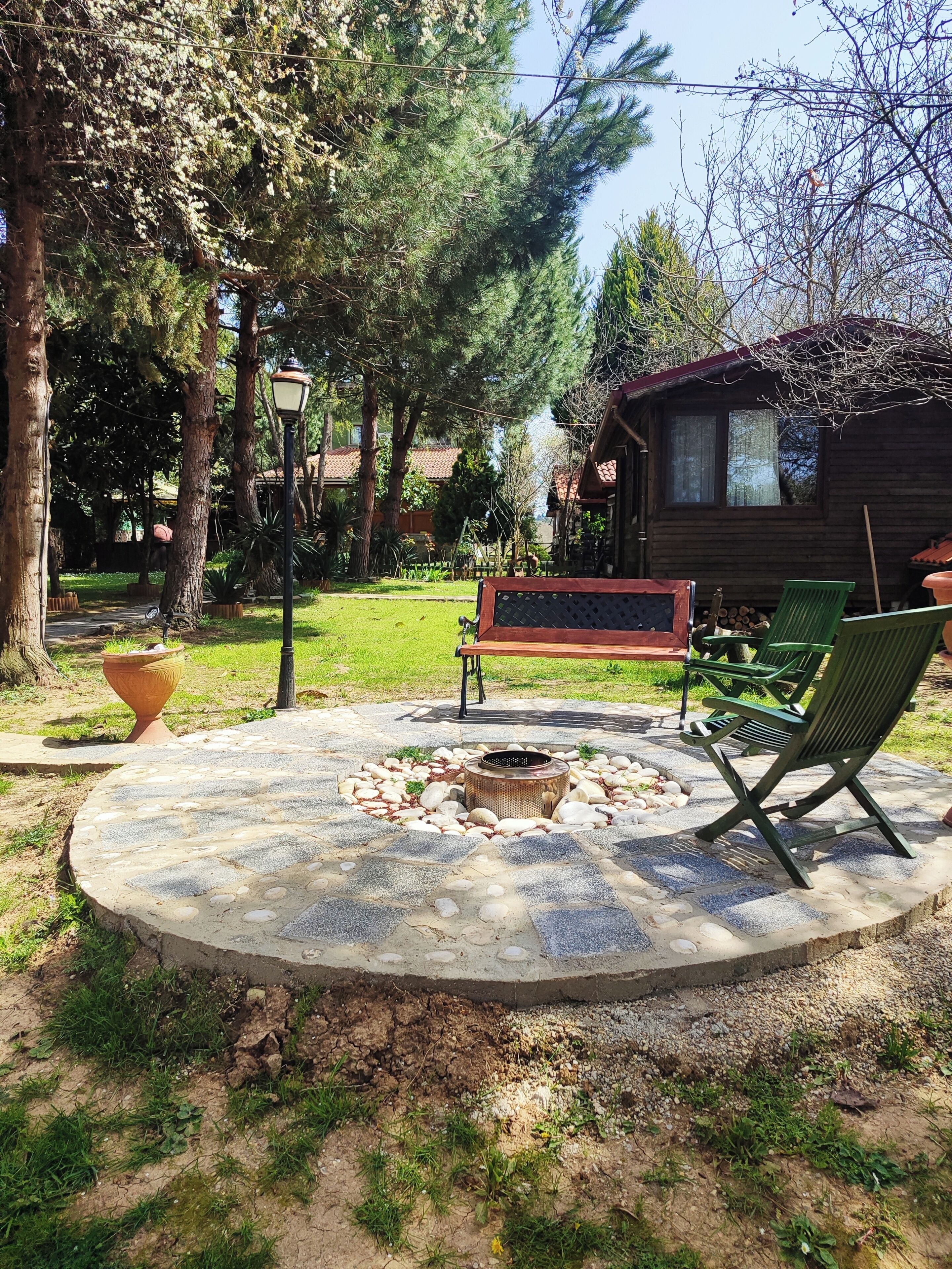 Un espacio circular al aire libre con una fogata, un banco y sillas verdes.