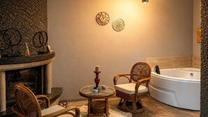 A bathroom with a stone wall, a bathtub, wicker chairs, a glass table, and a wall-mounted light fixture. - Agva Tartaruga Motel (Sile)