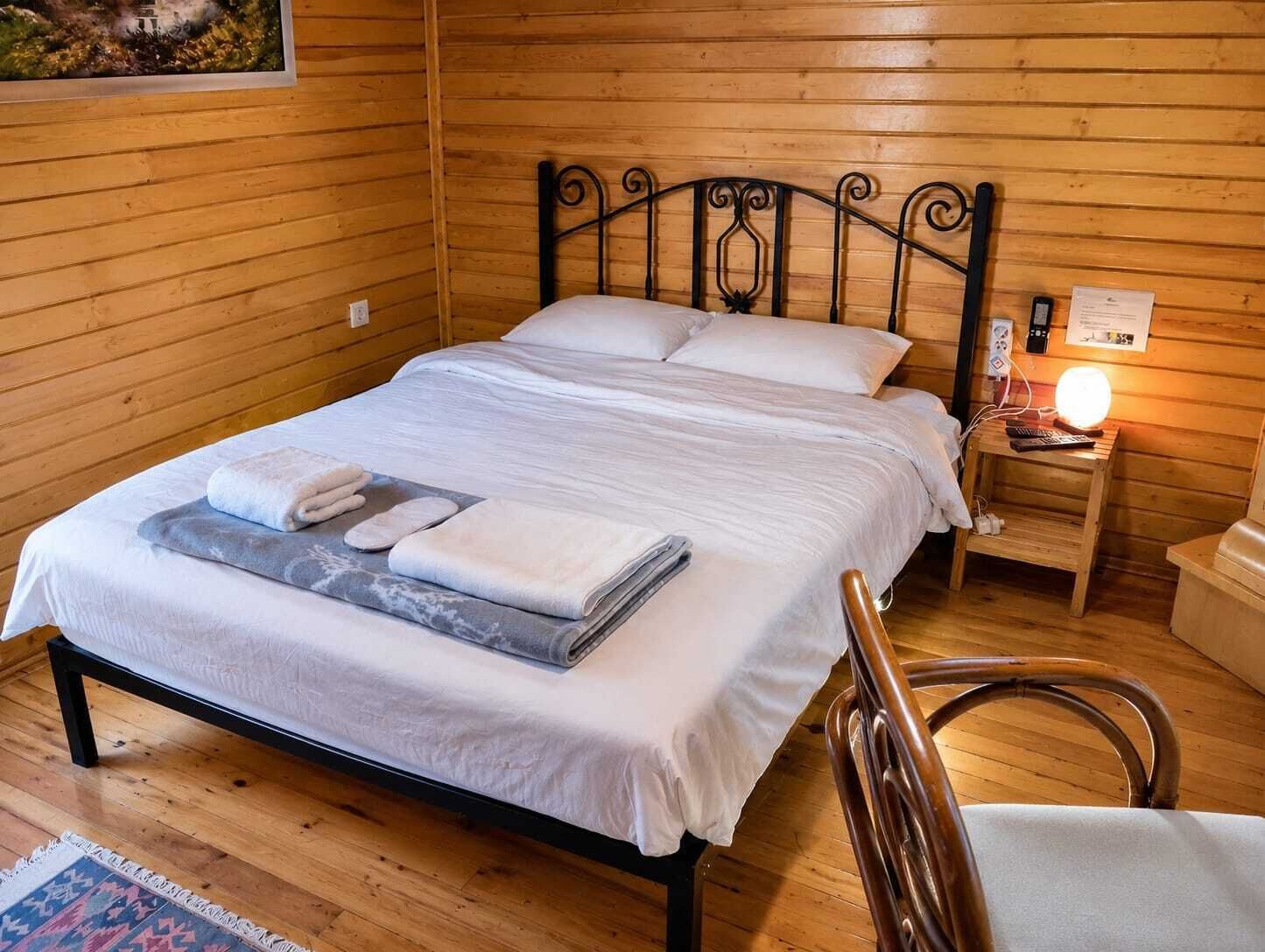 A wooden-paneled room with a bed, a nightstand with a lamp, and a chair.