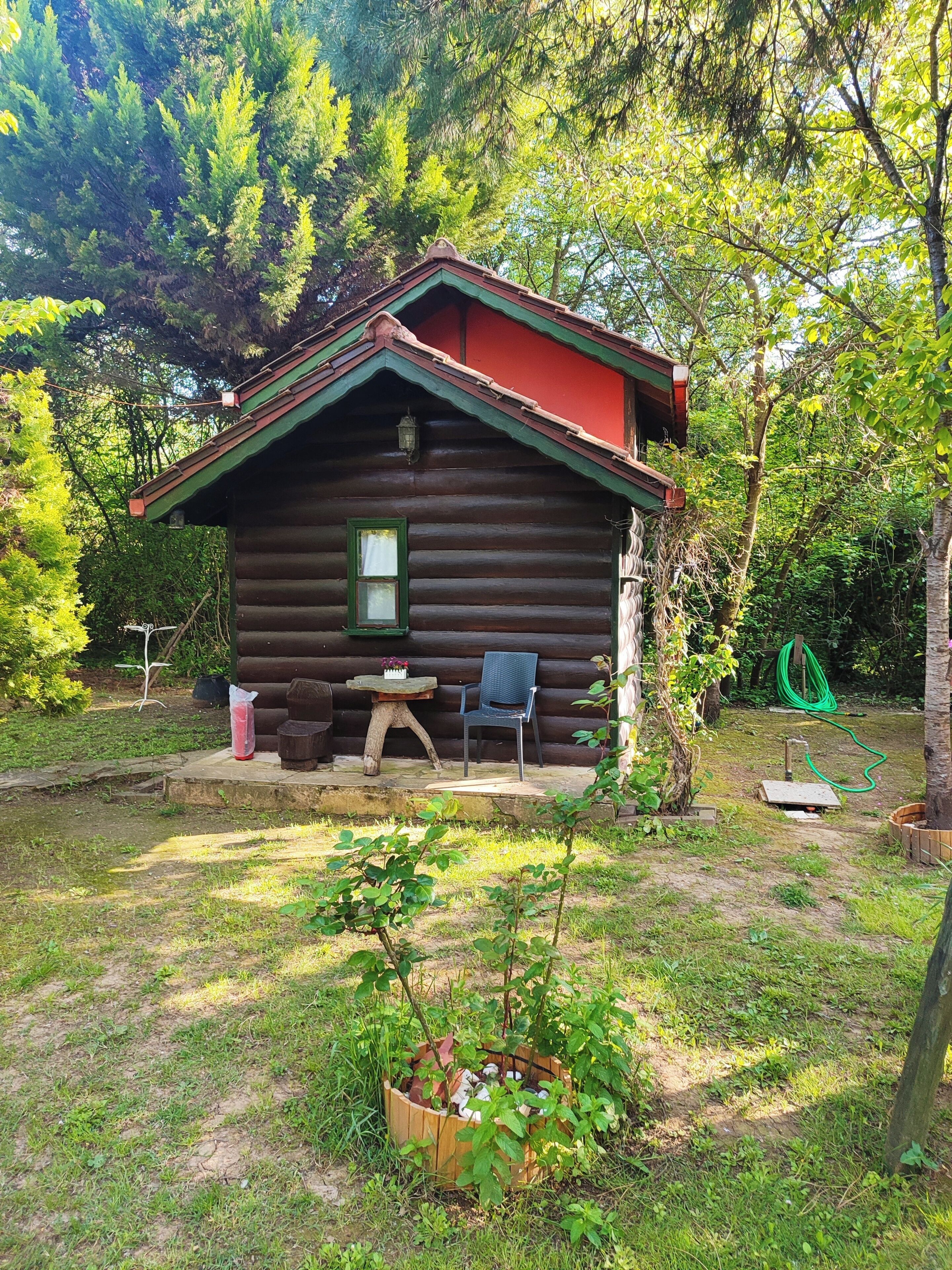 A log cabin with a red roof, a small porch, a table, and a chair.