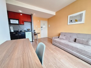 A modern living room with a sofa, a dining table, and a kitchen area with red cabinets and a microwave. - LK Barro Preto 11 (Belo Horizonte)