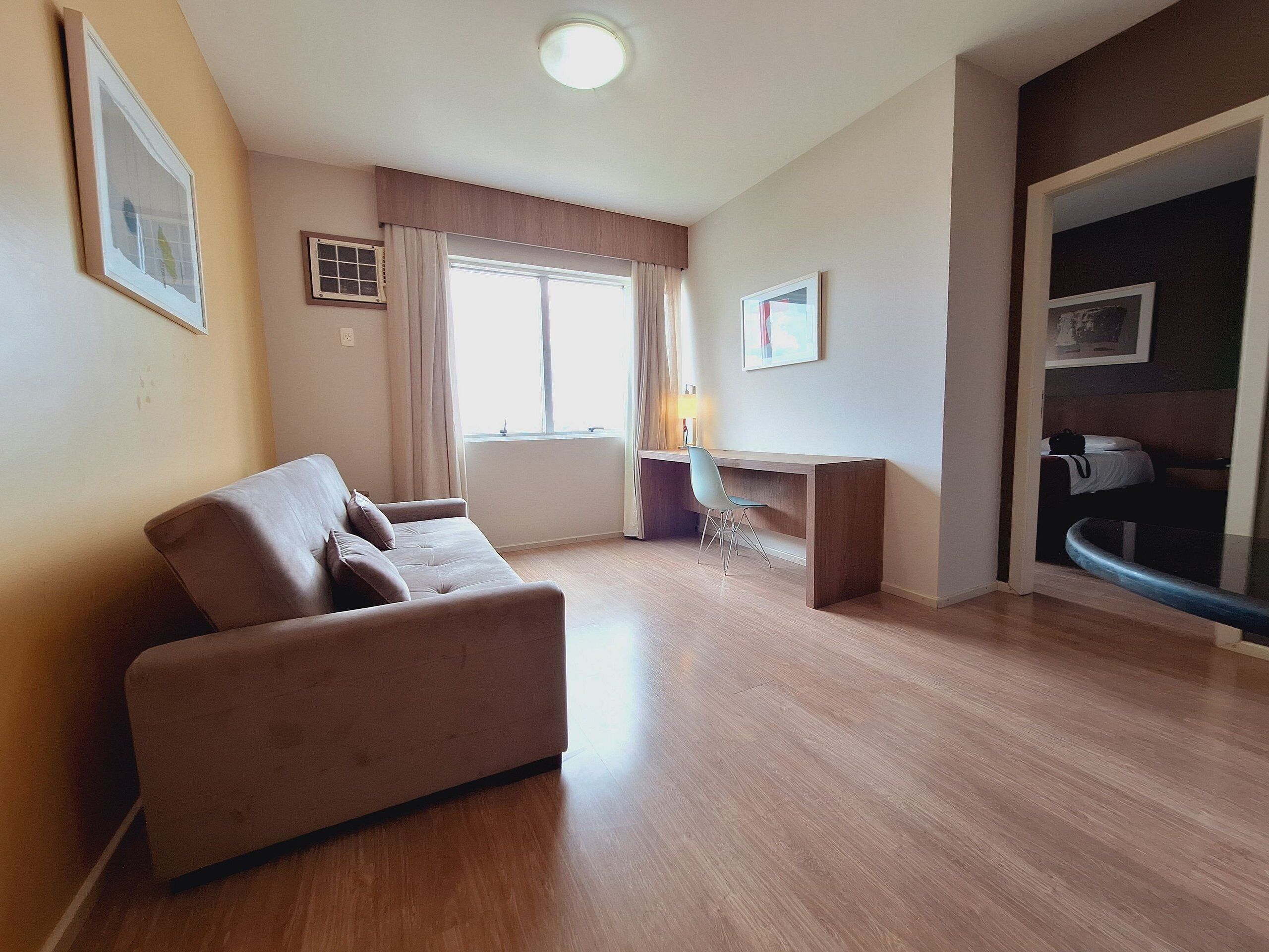 A modern living room with a sofa, a desk, and a bed in the background.