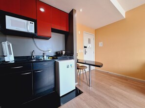 A kitchen with red cabinets, a white microwave, a small refrigerator, and a bar stool. - LK Barro Preto 11 (Belo Horizonte)