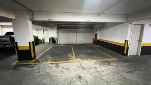 Un estacionamiento con pisos de concreto, líneas amarillas delimitando los espacios y paredes blancas con franjas amarillas.