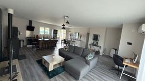 Una sala de estar moderna con un sofá gris, una mesa de centro de madera, un televisor y un comedor con una cocina al fondo.