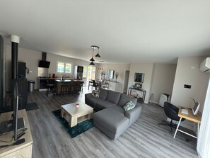 A modern living room with a grey sofa, a wooden coffee table, a TV, and a dining area with a kitchen in the background. - 🌴 Holiday home in Talais not far from Soulac- Terrace, small swimming pool (Talais)