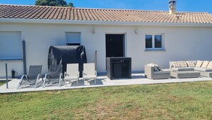 Una casa con techo de tejas, un área de estar al aire libre techada con sillas y un sofá, y una parrilla cubierta.