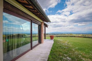 Ein modernes Gebäude mit großen Glasfenstern, einer Ziegelstütze und Blick auf eine grüne Landschaft.