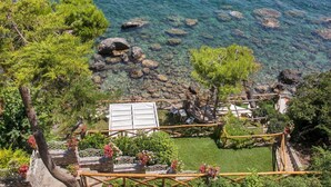 Un jardín costero con agua cristalina, rocas y una terraza de madera con asientos.