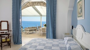 Un dormitorio con cama, escritorio, silla, mesita de noche y vista al mar.