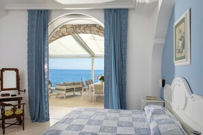 A bedroom with a bed, a desk, a chair, a nightstand, and a view of the sea. - Villa Infinity by My Villa Collection (Massa Lubrense)