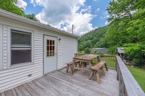 A wooden deck with a table and benches, a door with a window, and a view of a forested hillside.