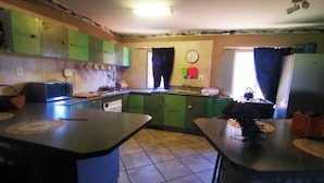 A kitchen with green cabinets, a microwave, a sink, and a clock on the wall.