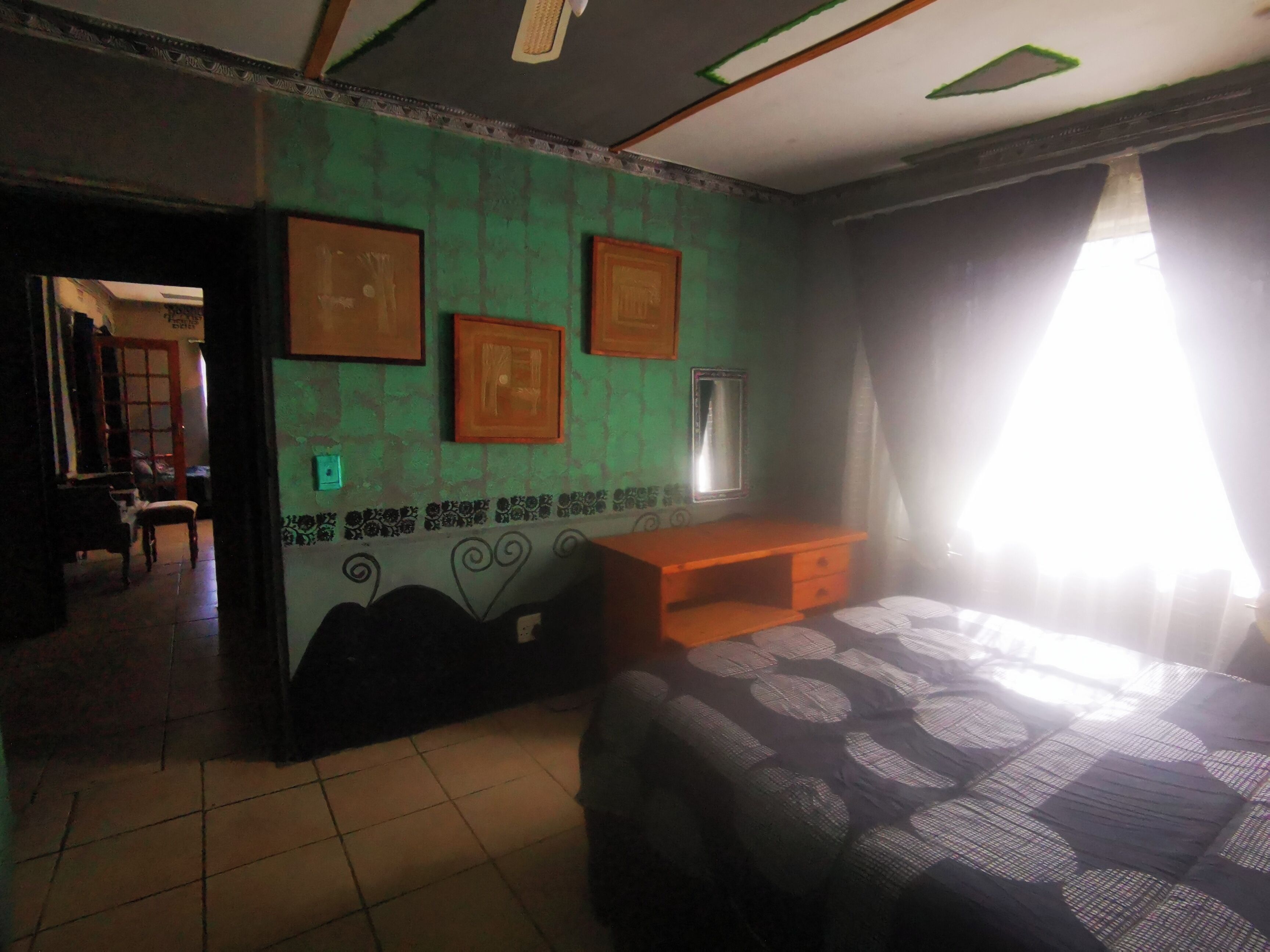 A room with a bed, a desk, a chair, and a door leading to another room.