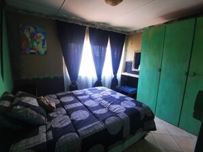 A bedroom with a bed, curtains, a green wardrobe, and a wall painting. - The Wagon Wheel Family Guest House (Chrissiesmeer)