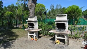Two outdoor pizza ovens with a tree and greenery in the background. - Modern Ground-floor Flat Near the Shores-bibione (San Michele al Tagliamento)