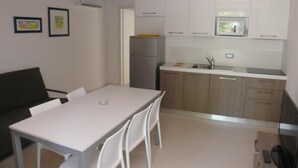 A compact kitchen with white cabinets, a refrigerator, and a microwave. There is a dining table with chairs. - Modern Ground-floor Flat Near the Shores-bibione (San Michele al Tagliamento)