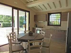 A modern kitchen with a dining area, featuring a large window, built-in cabinets, and a central island. - Panoramic villa with pool in Montaione (Montaione)