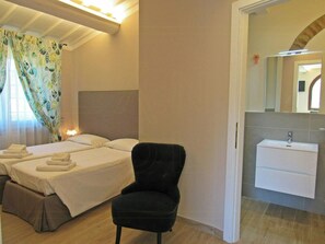 A hotel room with two beds, a black chair, a bedside table, a nightstand, a mirror, and a bathroom with a sink and mirror. - Panoramic villa with pool in Montaione (Montaione)