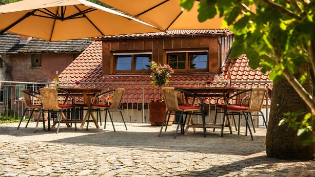 Un patio con mobiliario exterior, una sombrilla grande y un edificio con tejado de baldosas.