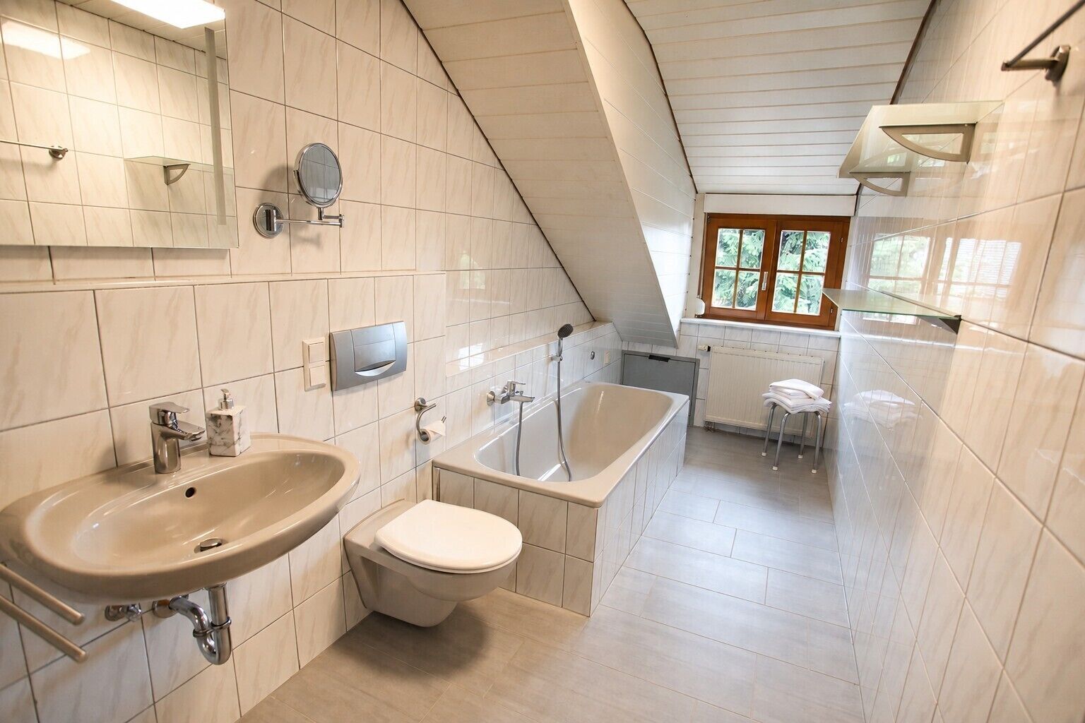 A modern bathroom with a sink, toilet, and bathtub, featuring white tiles and a sloped ceiling.