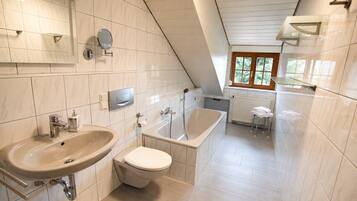 A modern bathroom with a sink, toilet, and bathtub, featuring white tiles and a sloped ceiling.
