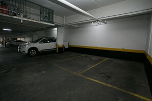 Un aparcament subterrani amb sòls de formigó, places d'aparcament senyalitzades i un cotxe blanc estacionat en una d'elles.