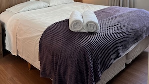 Una habitación de hotel con una cama, un cuadro en la pared, una ventana con cortinas y un aire acondicionado instalado en la pared.