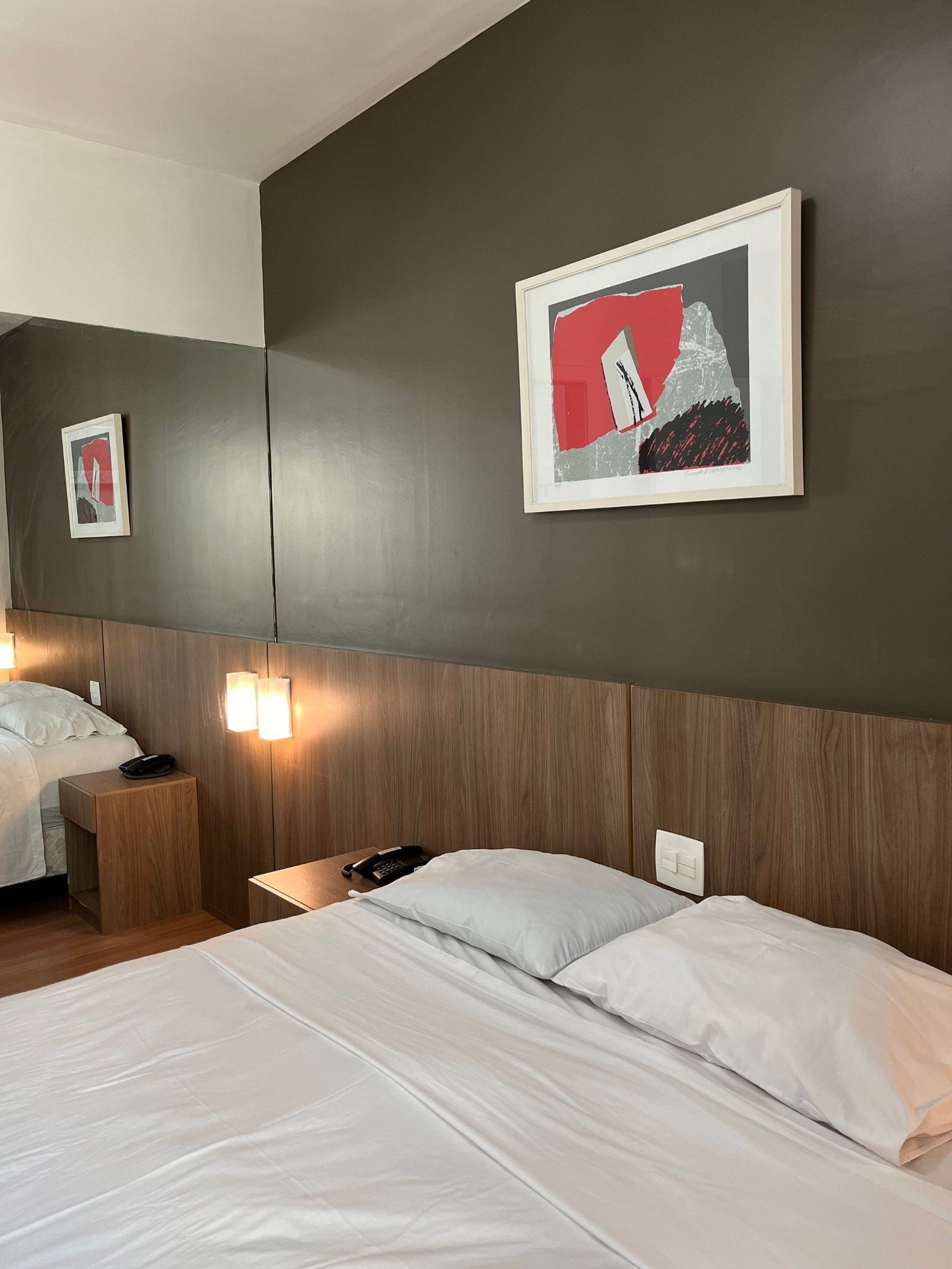Habitación de hotel con una cama grande, mesitas de noche, un teléfono y lámparas fijadas a la pared.