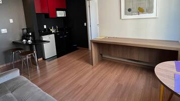A modern living room with a grey sofa, a wooden coffee table, and a kitchen area with red cabinets and a microwave.