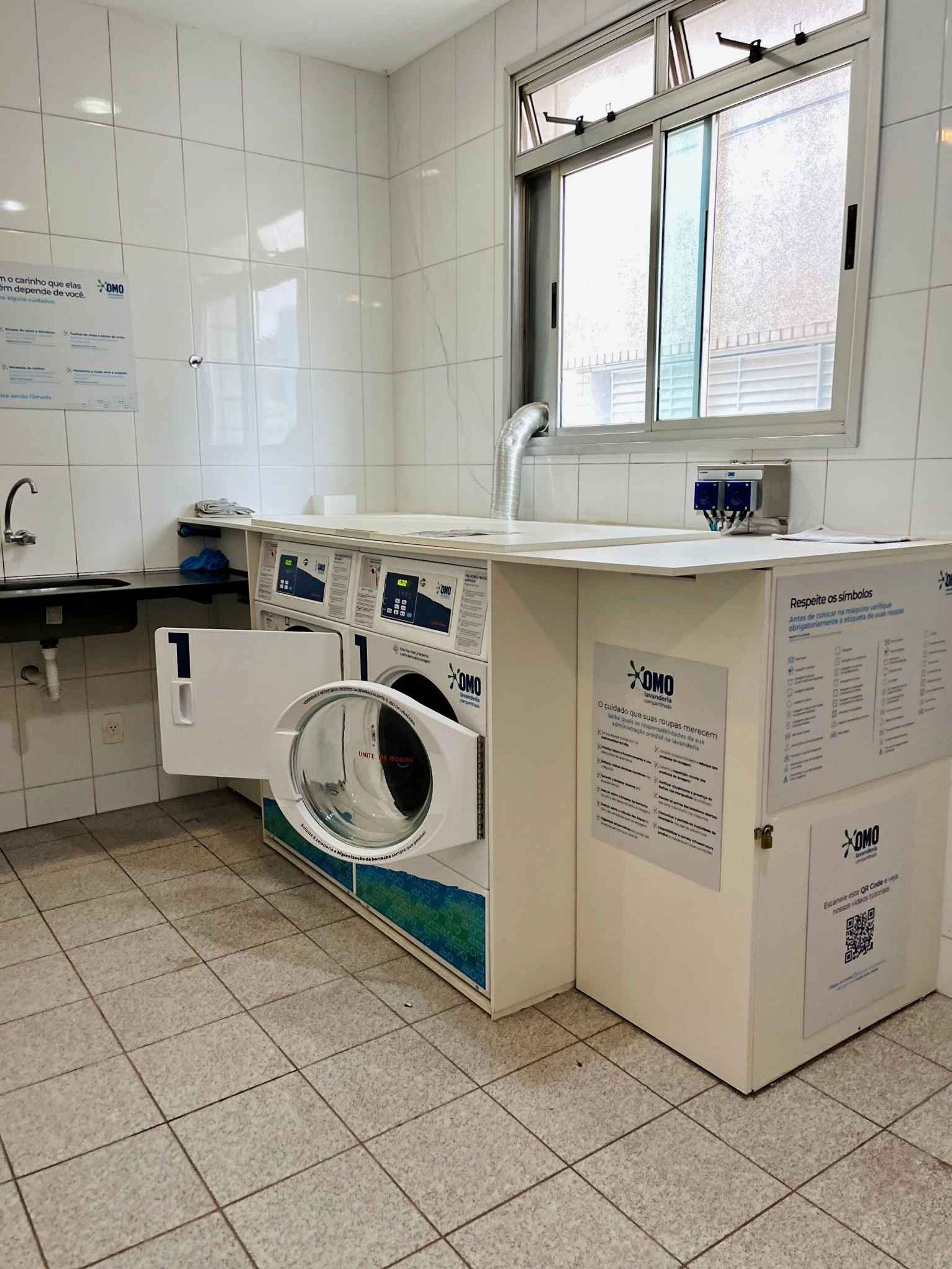 A laundry facility with a washing machine, a sink, and informational posters.