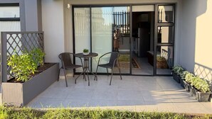A patio with a table and chairs, a small plant, and a sliding glass door leading to a kitchen. - Stylish Stay at 11 on Arch in Langebaan, South Africa (Langebaan)