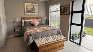A bedroom with a bed, bedside tables, a wooden bench, a ceiling fan, and a window with blinds. - Stylish Stay at 11 on Arch in Langebaan, South Africa (Langebaan)