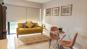 A modern living room with a yellow sofa, a glass dining table, and a patterned rug. - Stylish Stay at 11 on Arch in Langebaan, South Africa (Langebaan)
