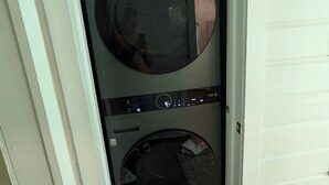 Une buanderie équipée d’un lave-linge et d’un sèche-linge LG, d’un miroir rond et d’un petit tapis sur le sol.