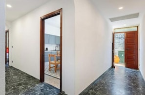 Un pasillo con una puerta de madera que da a una zona de cocina con una silla y una mesa.